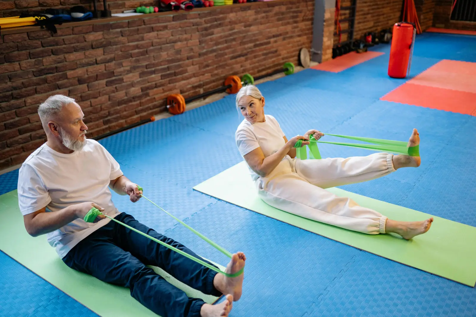 Senior couple exercising with resistance bands on yoga mats in a gym