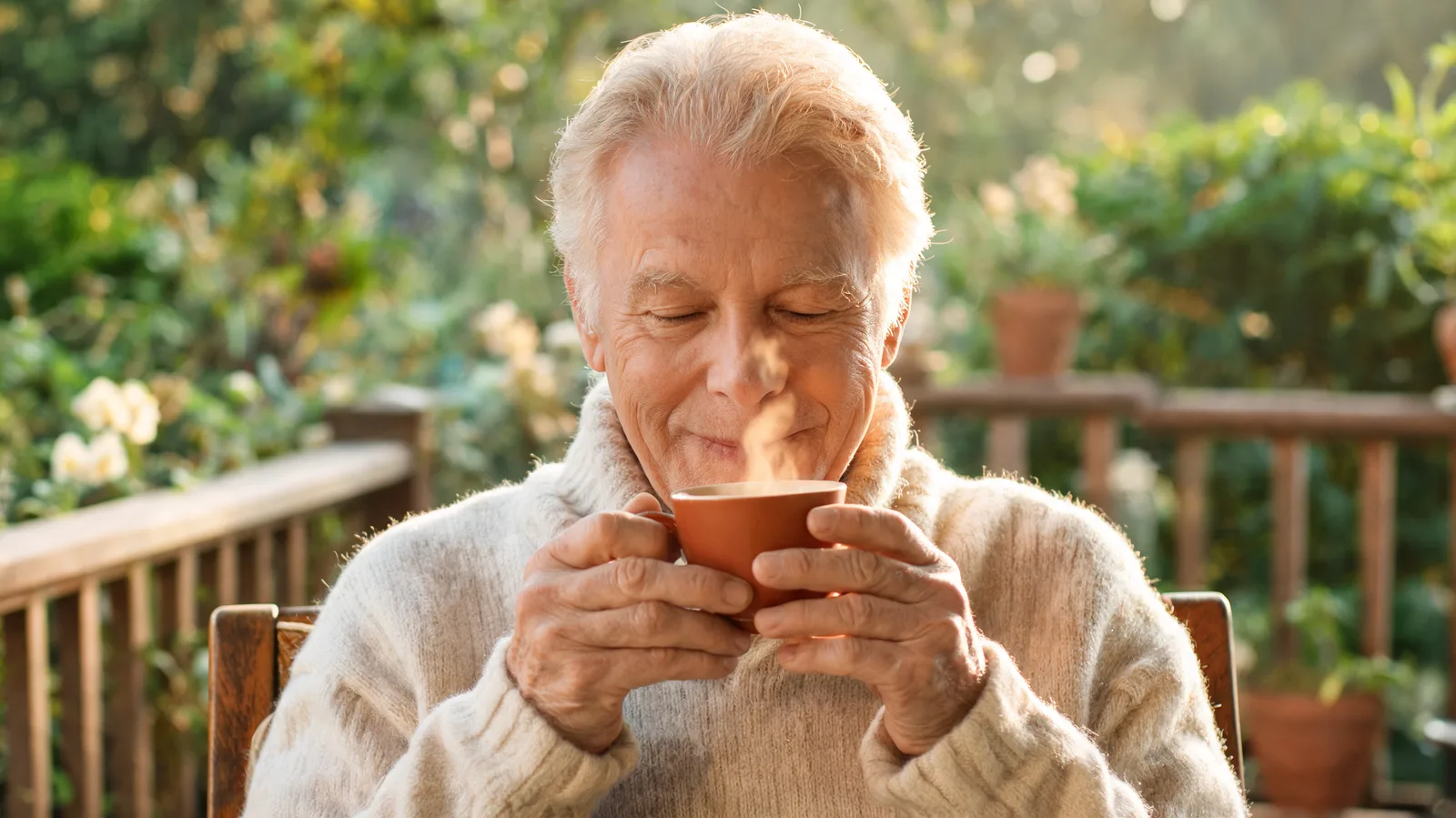 An older man with a cup of morning tea on his porch as the sun rises.