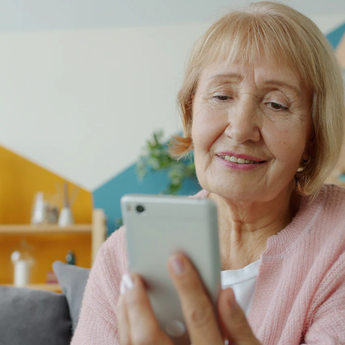 Senior woman smiling warmly while using her smartphone at home, representing friendly and accessible support